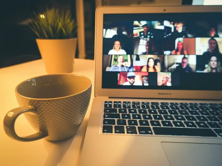 A laptop showing a large video meeting next to a coffee mug